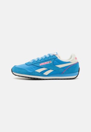 Baskets Reebok bleu et blanc avec des touches roses, tige en daim et tissu, logo visible et semelle en caoutchouc noir, vue de côté.