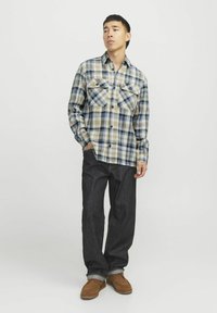 Kariertes Flanellhemd in Blau, Beige und Braun mit zwei Brusttaschen, Knopfverschluss und langen Ärmeln. Kombiniert mit dunkelblauen Jeans und braunen Schuhen.