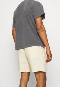 Harmaa puuvillapaita lyhyillä hihoilla ja rennolla istuvuudella, yhdistettynä vaaleankeltaisiin pellavashortseihin, joissa on tasku ja rento leikkaus.