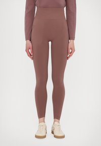 Slim-fit high-waist mauve leggings with side zip pocket, worn with matching mauve top and beige sneakers on white background.