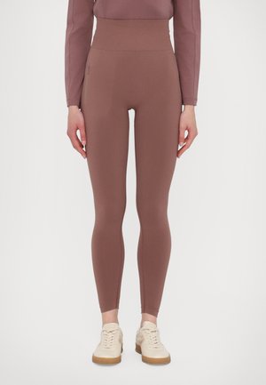 Slim-fit korkeavyötäröiset mauve-kankaat, joissa on sivutasku vetoketjulla, yhdistettynä matching mauve-paitaan ja vaaleanbeigeihin lenkkareihin valkoisella taustalla.