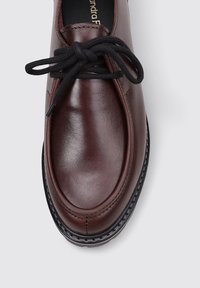 Zapato de cuero marrón con punta redondeada, que presenta cordones negros y una suela texturada acentuada por costuras visibles a lo largo de los bordes.