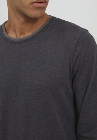 Donkergrijze lange mouwen t-shirt van zachte katoen. Heeft een ronde halslijn met een contrasterende lichtgrijze rand. Eenvoudig ontwerp.