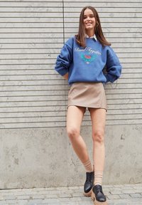 Sweatshirt bleu avec le texte "Bond Together" et un graphisme. Jupe mini en simili-cuir beige. Chaussures à plateforme noires avec lacets, chaussettes côtelées.