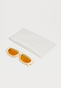 Occhiali da sole con una montatura in plastica color crema chiaro e lenti arancioni, accompagnati da una custodia in pelle bianca con rilievo.