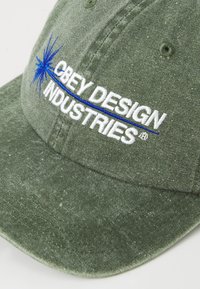 Olive green fabric cap with white embroidered text "OBEY DESIGN INDUSTRIES" and a blue starburst graphic above the text.