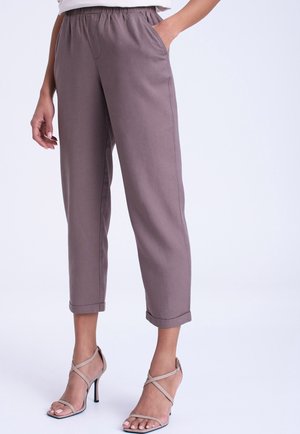 Parte inferior del cuerpo de una persona que lleva pantalones cortos ajustados color malva con cintura elástica y sandalias beige de tacón alto con tiras en el tobillo.