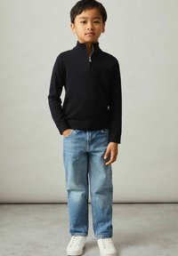 Maglione nero mezza zip, jeans in denim blu, sneakers bianche. Outfit casual con un design aderente e tessuto testurizzato.