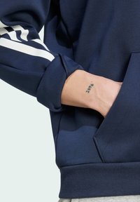 Námořnická modrá mikina s dlouhými rukávy, bílé pruhy na rukávech a klokanka. Vyrobeno z měkké tkaniny s žebrovanými manžetami.