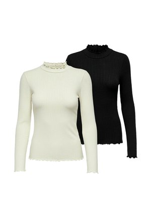 Woman standing wearing a beige long-sleeve top, loose black pants with gathered hems, and black high-heeled ankle boots on a white background.