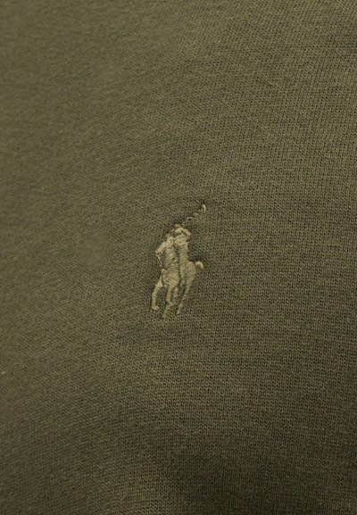 Bordado de um jogador de polo a cavalo segurando um taco levantado em tecido malha verde-oliva.