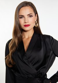 Accappatoio in satin nero con design avvolgente, caratterizzato da un profondo scollo a V e maniche lunghe. Accentuato da una vita legata e una leggera lucentezza. Orecchini a cerchio dorati.