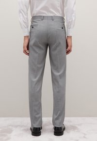 Grijze pantalon met een gestructureerd patroon, voorzien van achterzakken met zwarte knopen. Gestyled met een wit overhemd en zwarte schoenen.