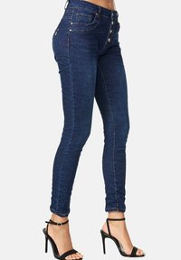 Jeans ajustados de color azul oscuro con una cintura alta, que cuentan con un cierre de cinco botones y bolsillos delanteros y traseros. Textura de denim suave con costuras mínimas.