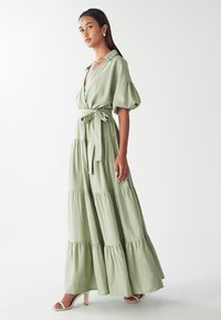 Svetlozelené maxi šaty s tierovaním, krátkymi puff rukávmi a viazaním v páse. Hladká tkanina s voľným strihom a vertikálnymi švami.