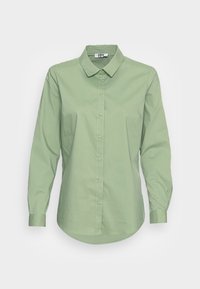 Ljusgrön långärmad skjorta med knappar och krage, som har en mjuk textur och en rundad nederkant. Knapparna fram lyfter fram designen.