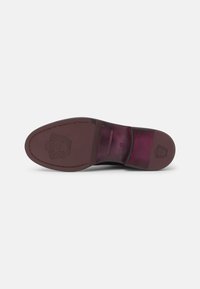 Semelle de chaussure en cuir noir avec des accents bordeaux, présentant un logo embossé et des coutures détaillées le long des bords. Texture lisse, finition légèrement brillante.