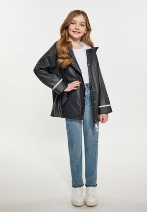 Sort vandtæt jakke med hætte, reflekterende striber og trykknapper. Kombineret med lyseblå jeans og hvide sneakers.