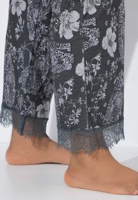 Grå pyjamasbukser med et leopard- og blomsterprint i sort og hvid, udstyret med en dekorativ grå blondekant nederst.