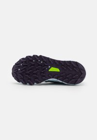 La semelle d'une chaussure présente un motif de crampons profond et texturé pour une meilleure adhérence, de couleur violette avec un accent vert vif et des bordures blanches.