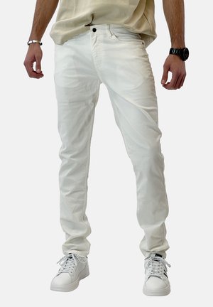 Jeans de mezclilla blanca ajustados, con bolsillos frontales, cierre de botón y una textura sutil, combinados con zapatillas blancas.
