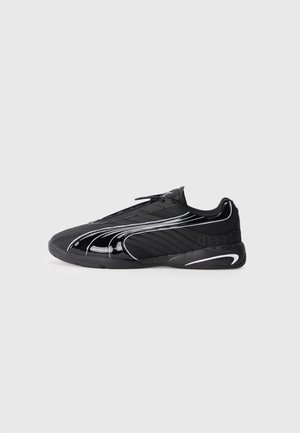 Chaussure de sport basse noire avec un design rayé brillant et des accents blancs, montrée de profil sur un fond uni clair.