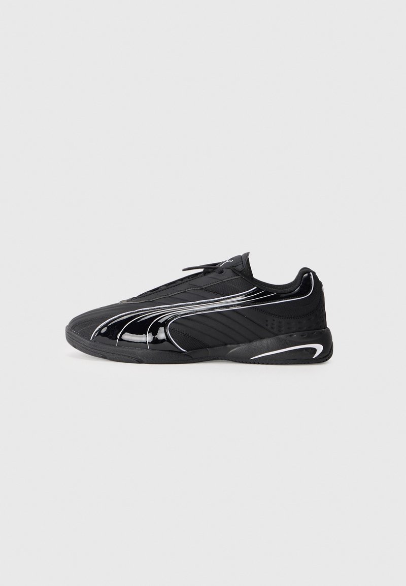 Chaussure de sport basse noire avec un design rayé brillant et des accents blancs, montrée de profil sur un fond uni clair.