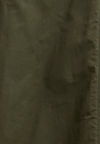 Υφάσμα σε σκουροπράσινο ελιάς με διακριτικές ζάρες και ραμμένη κάθετη ραφή στη δεξιά πλευρά.