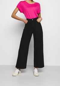 Camiseta de manga corta fucsia combinada con pantalones de pierna ancha negros de cintura alta y zapatillas blancas. Tejido suave y corte relajado.