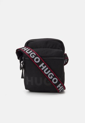 Sac bandoulière noir en tissu résistant, doté d'un compartiment zippé et d'une large bandoulière avec le logo "HUGO" répété en blanc et rouge.