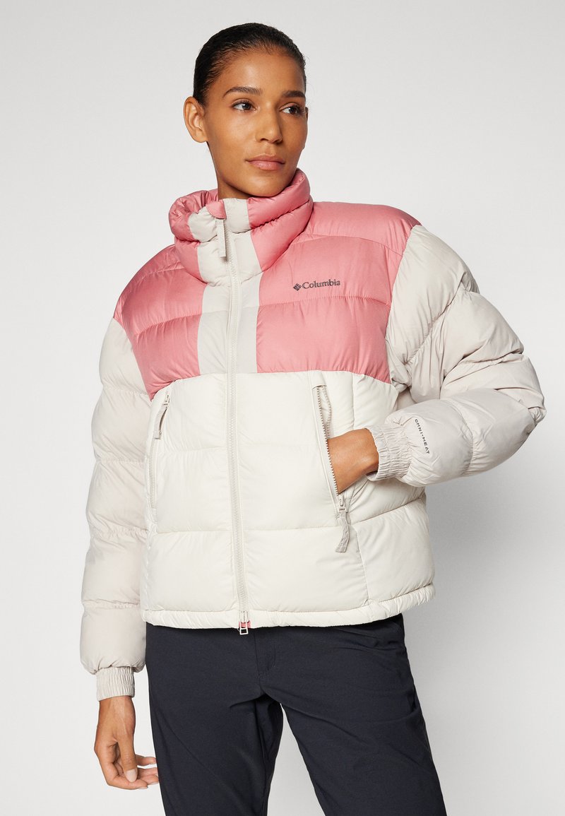 Chaqueta tipo plumas con un diseño de bloques de color rosa y blanco. Cuenta con un cuello alto, bolsillos con cremallera y puños elastizados. Textura suave y acolchada.