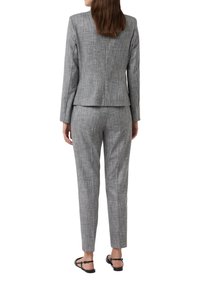 Grijze gebreide blazer en bijpassende broek, slim fit ontwerp, rechte pijpen, minimale hardware, gedragen met platte zwarte sandalen.