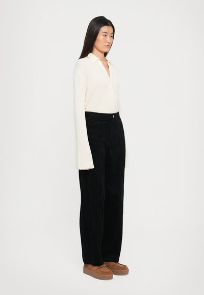 Krems krāsas ribota garām piedurknēm polo krekls, melnas teksturētas platajās kājstarpes bikses un brūni platformas apavi. Vienkāršs dizains un neitrālas krāsas.