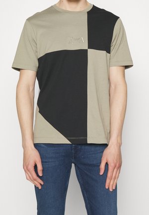 T-shirt à manches courtes en kaki et noir, avec un design à blocs de couleurs géométriques et un petit logo embossé sur la poitrine. Matière en coton.