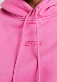 Sweat à capuche rose en mélange de coton doux. Il comporte une poche kangourou, des cordons de serrage et un logo Levi's brodé assorti en rose.