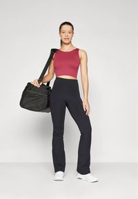 Atletska oprema z rebrasto bordo kratko majico in visokim pasom ter črnimi širokimi hlačami; kombinirano s črno športno torbo in belimi supergami.