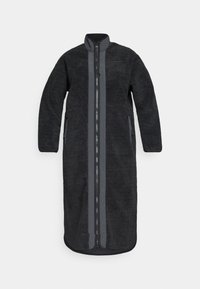Zwarte lange jas van pluizig fleece, met een voorrits, twee zijzakken en effen grijze accenten langs de rits en mouwen.