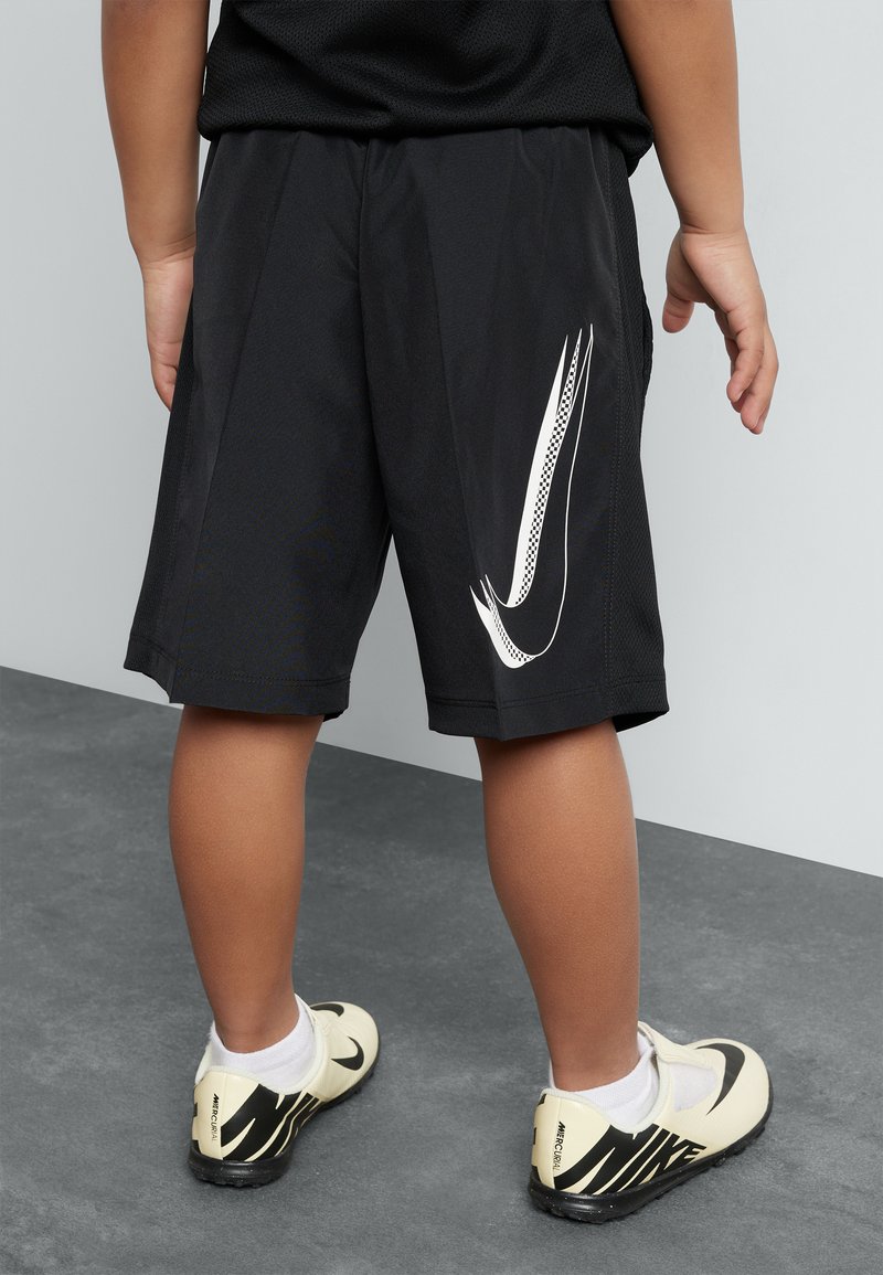 Black athletic shorts with a white Nike logo, featuring a lightweight mesh fabric and side pockets. Complemented by beige and black shoes.