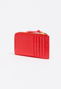 Cartera roja con textura de cocodrilo y cierre de cremallera. Presenta múltiples compartimentos para tarjetas y un acabado suave. Herrajes de cremallera en tono dorado. Diseño compacto.