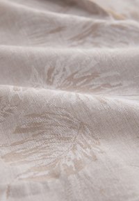 Tela beige claro con sutiles patrones tejidos de hojas y pliegues suaves que crean una textura y profundidad delicadas.