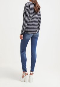 Pruhované dlouhé rukávy v námořnické modré a bílé, kombinované s modrými slim kalhotami a bílými platformovými sandály. Outfitu je neformální a těsně padnoucí.