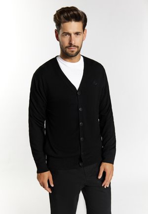 Cardigan negru cu decolteu în V, cu șapte butoane în față și manșete cu dungi. Purtați peste un tricou alb, care are un logo mic pe piept.