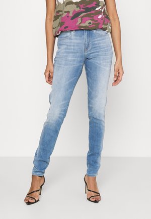 Jean skinny en denim bleu clair avec une finition délavée, présentant un design traditionnel à cinq poches et une taille mi-haute.