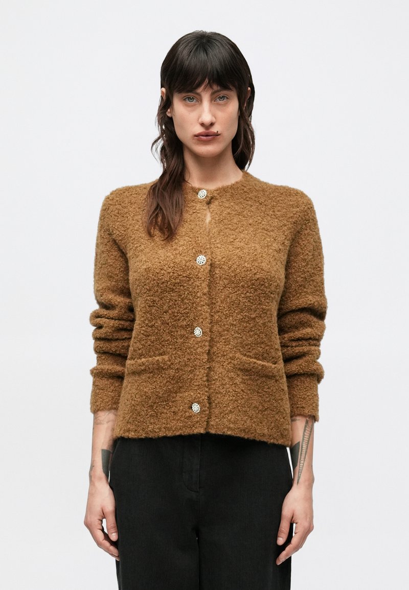 Brązowy, teksturowany kardigan z okrągłym dekoltem, długimi rękawami i przednimi kieszeniami, ozdobiony błyszczącymi srebrnymi guzikami wzdłuż środka.