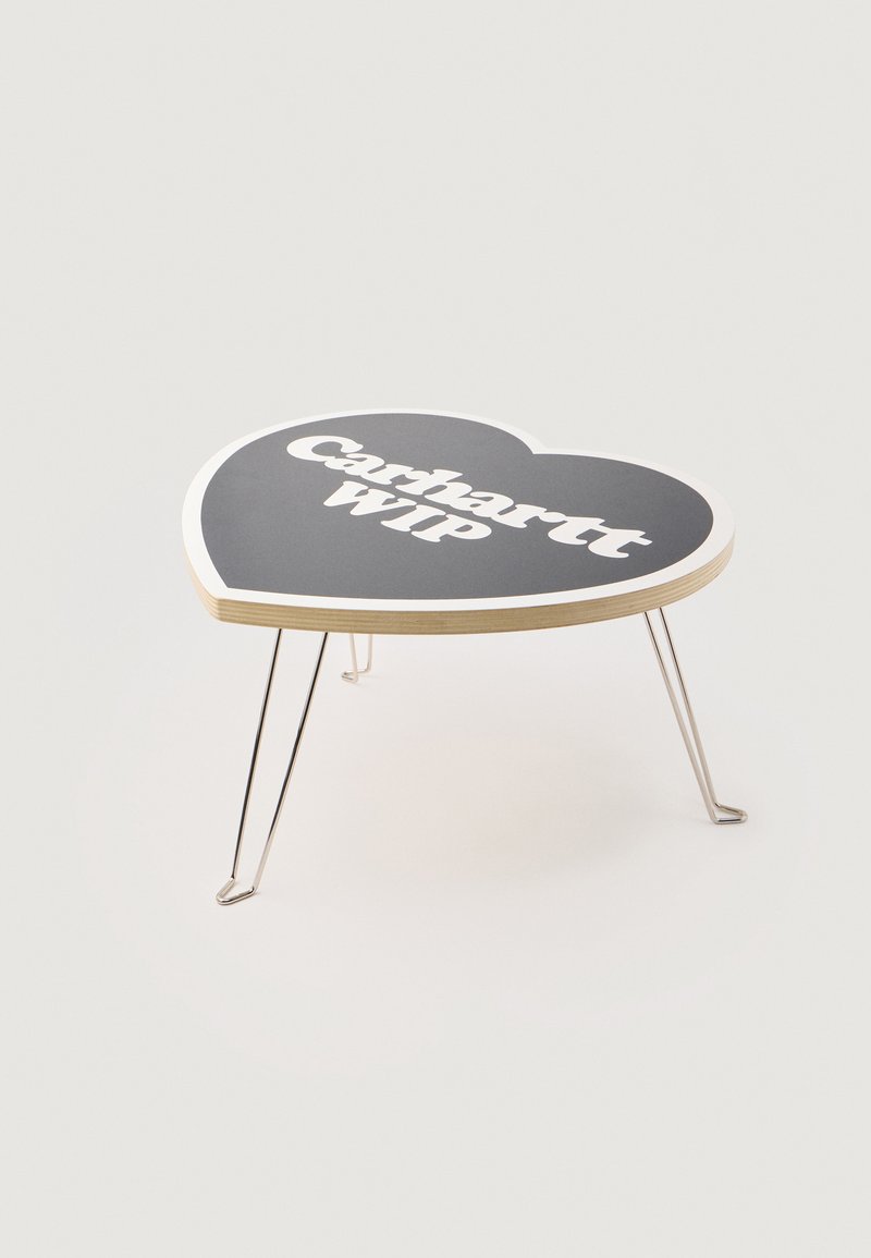 Hartvormige tafel met een zwarte bovenkant waarop "Carhartt WIP" in witte tekst is afgebeeld, ondersteund door dunne metalen poten. Glad oppervlak en afgeronde hoeken.