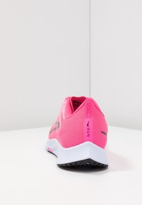 Zapatilla deportiva rosa con parte superior de malla transpirable, acentos negros, una media suela blanca y una suela exterior negra texturizada. Presenta un detalle de logotipo.