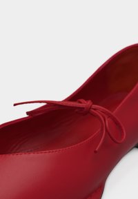 Κόκκινη μπαλαρίνα από δέρμα με στρογγυλή μύτη και δεμένη φιόγκο στην κορυφή, απεικονισμένη σε λευκό φόντο, σε γωνιακή όψη.