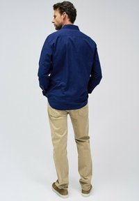 Camisa de botones azul marino de manga larga, combinada con chinos beige y zapatos marrón claro. Textura suave y corte clásico.