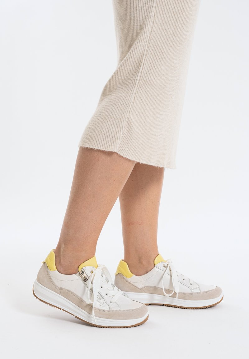 Weiße und beige Sneakers mit gelben Akzenten, mit einem Design aus Wildleder und Mesh, runder Zehenpartie und flacher Gummisohle. Die Schnürsenkel sind sichtbar.