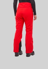 Pantalon de ski rouge imperméable avec taille haute, accents noirs au niveau des chevilles et texture lisse. Présente des jambes longues et une coupe décontractée.